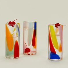 three different colored vases sitting next to each other on a white surface with cherries in them