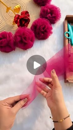 two hands are holding pink sheer ribbon near some flowers and scissors on a white surface