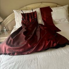 a red dress is laying on top of a white bed with pillows and pillow cases