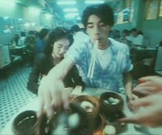 two people sitting at a table with food in front of them and one person reaching for something