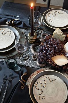 the table is set with black and white plates, silverware, candlesticks and crackers