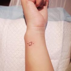 a small saturn tattoo on the wrist