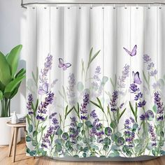 a shower curtain with purple flowers and butterflies on it, next to a potted plant