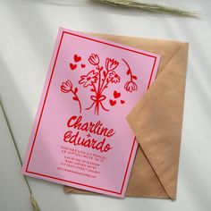 a pink card with red flowers and hearts on it is next to a brown envelope