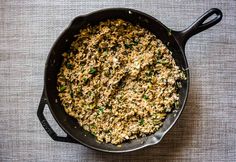 a skillet filled with food sitting on top of a cloth covered table next to a wooden spoon