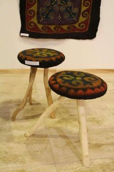 two wooden stools sitting next to each other in front of a rug on the wall