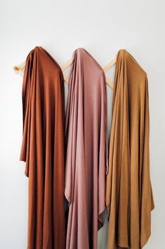 three scarves hanging on a wall with one draped over the other in different colors