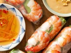 shrimp wrapped in paper next to dipping sauce and carrot sticks on a plate with other food items