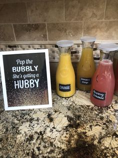 three bottles of juice sitting on top of a counter next to a sign that says pop the bubbly she's getting a hubby