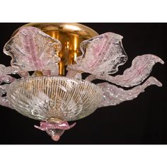 a pink glass chandelier hanging from a gold ceiling fixture with leaves on it