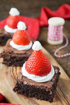 chocolate brownies with whipped cream and strawberries on top are sitting on a cutting board