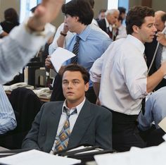 a group of men in business attire sitting at desks with papers and pens on their laps