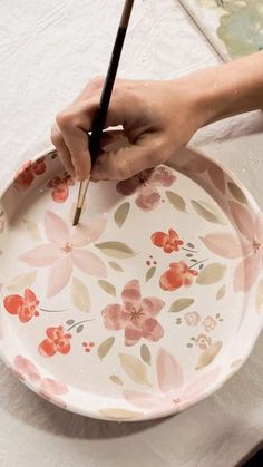 a person is holding a paintbrush and painting a flowered plate with flowers on it