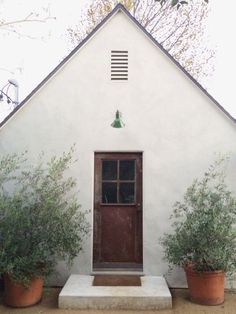 a small white building with two potted plants and a door on the front porch