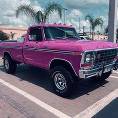 a pink pick up truck parked in a parking lot next to other cars and palm trees