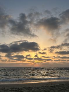 the sun is setting over the ocean with clouds in the sky and on the beach