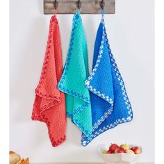 three colorful towels hanging on a wooden rack next to apples and bowl of cherries