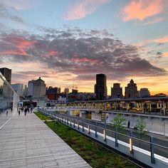 people are walking on the boardwalk in front of a cityscape at sunset or dawn