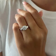 a woman's hand with a diamond ring on her left hand and a white t - shirt on the right