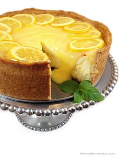 a cheesecake with lemons on top is sitting on a silver platter next to a green leaf