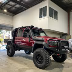 a red jeep parked in a garage next to a white building with windows on the roof