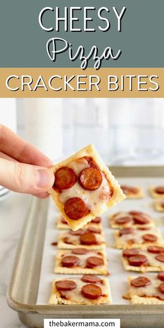 a hand holding a piece of pizza cracker bites over a baking pan with pepperoni on it