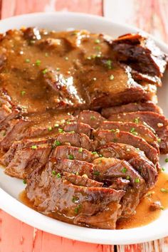 a white plate topped with meat and gravy on top of a wooden table