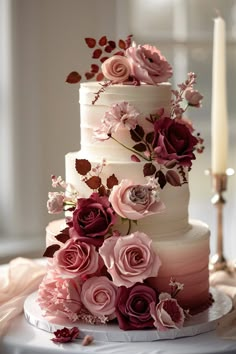 a three tiered cake with pink flowers on top and candles in the back ground