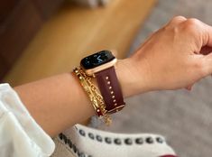 a woman is holding onto her apple watch with gold chains on the wrist and bracelet