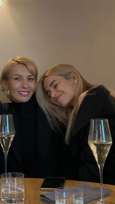 two women sitting next to each other at a table with wine glasses on the table