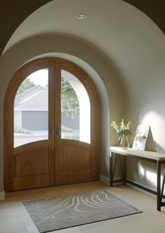 an arched wooden door in a white room with a rug on the floor next to it