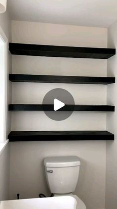 a white toilet sitting in a bathroom next to black shelves on the wall above it