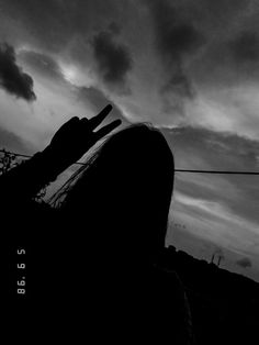 black and white photograph of a person holding their hand up to the sky with clouds in the background