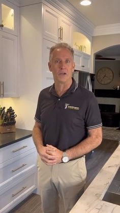 a man standing in a kitchen next to a counter with a clock on the wall