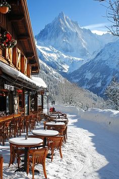 tables and chairs covered with snow in front of a mountain