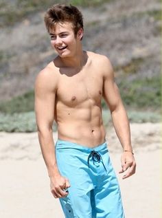 shirtless young man walking on the beach in blue shorts and no shirt, with his mouth open