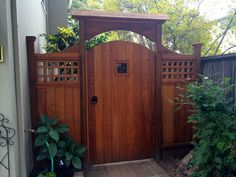 a wooden gate in front of a house with potted plants on the side walk