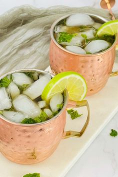 two copper mugs filled with ice, lime and mint garnish on a white tray