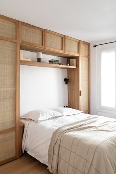 a bed with white sheets and pillows next to a wooden book shelf filled with books