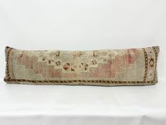 an old decorative pillow on a white tablecloth with a brown border around the edges