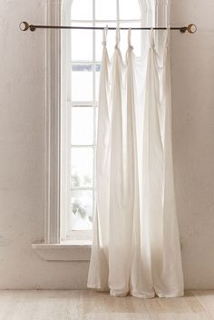 a white curtain hanging in front of a window with an arched window sill and wood flooring