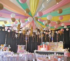 a room filled with lots of tables covered in white and pink paper lanterns hanging from the ceiling