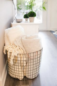 a basket filled with blankets sitting on top of a wooden floor next to a window