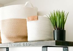 two large white baskets sitting on top of a shelf next to a potted plant