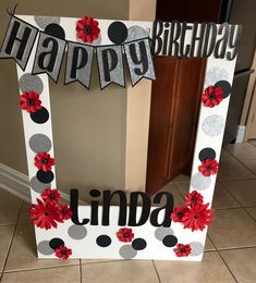 a happy birthday sign with red flowers and black polka dots on the bottom, sitting in front of a door