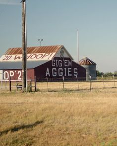 an old red barn sits in the middle of a field near a pole and telephone pole