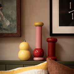 three different colored vases sitting on top of a bed next to a painting and pillow