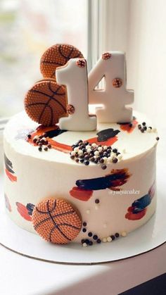 a decorated birthday cake with basketballs and balls on the top is sitting in front of a window