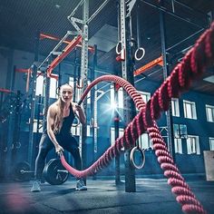 a woman doing exercises with a rope in a crossfit gym, surrounded by ropes