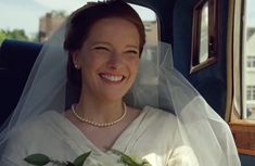 a woman in a white dress and veil smiles as she sits in the back of a car